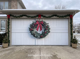 White garage door decorated for Christmas with a large wreath, garland, and red bows.